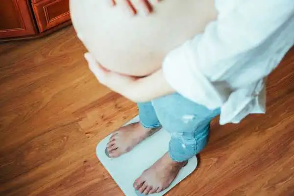 Image of woman weighing herself and experiencing weight gain through pregnancy Bordesley